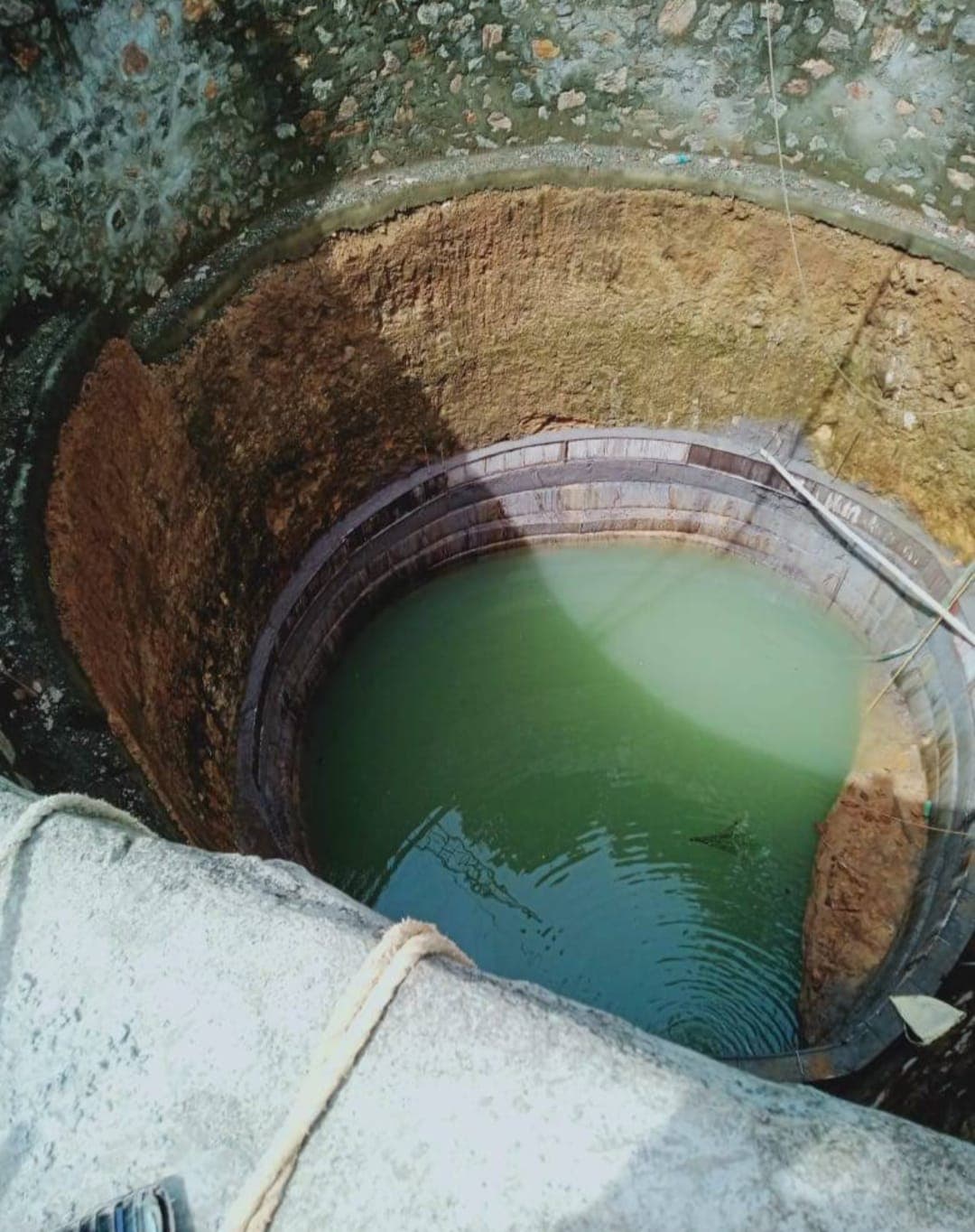 A deep, circular well with layered stone and earthen walls, containing murky green water.