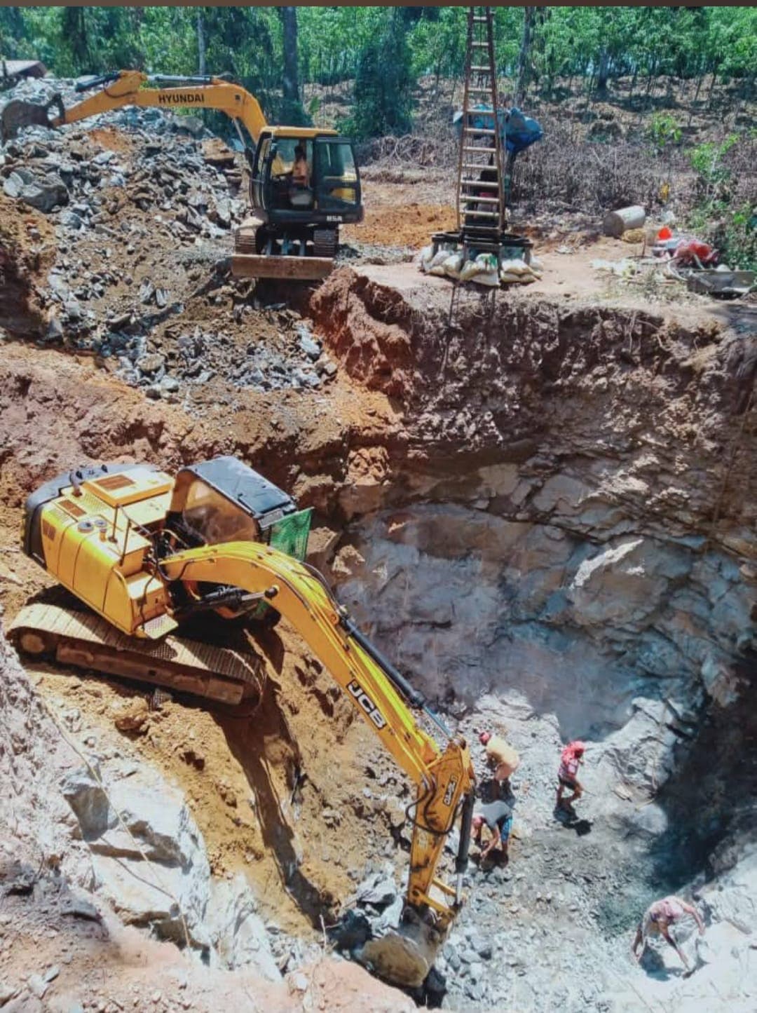 Two yellow excavators and workers digging a deep, rocky pit at a construction site.